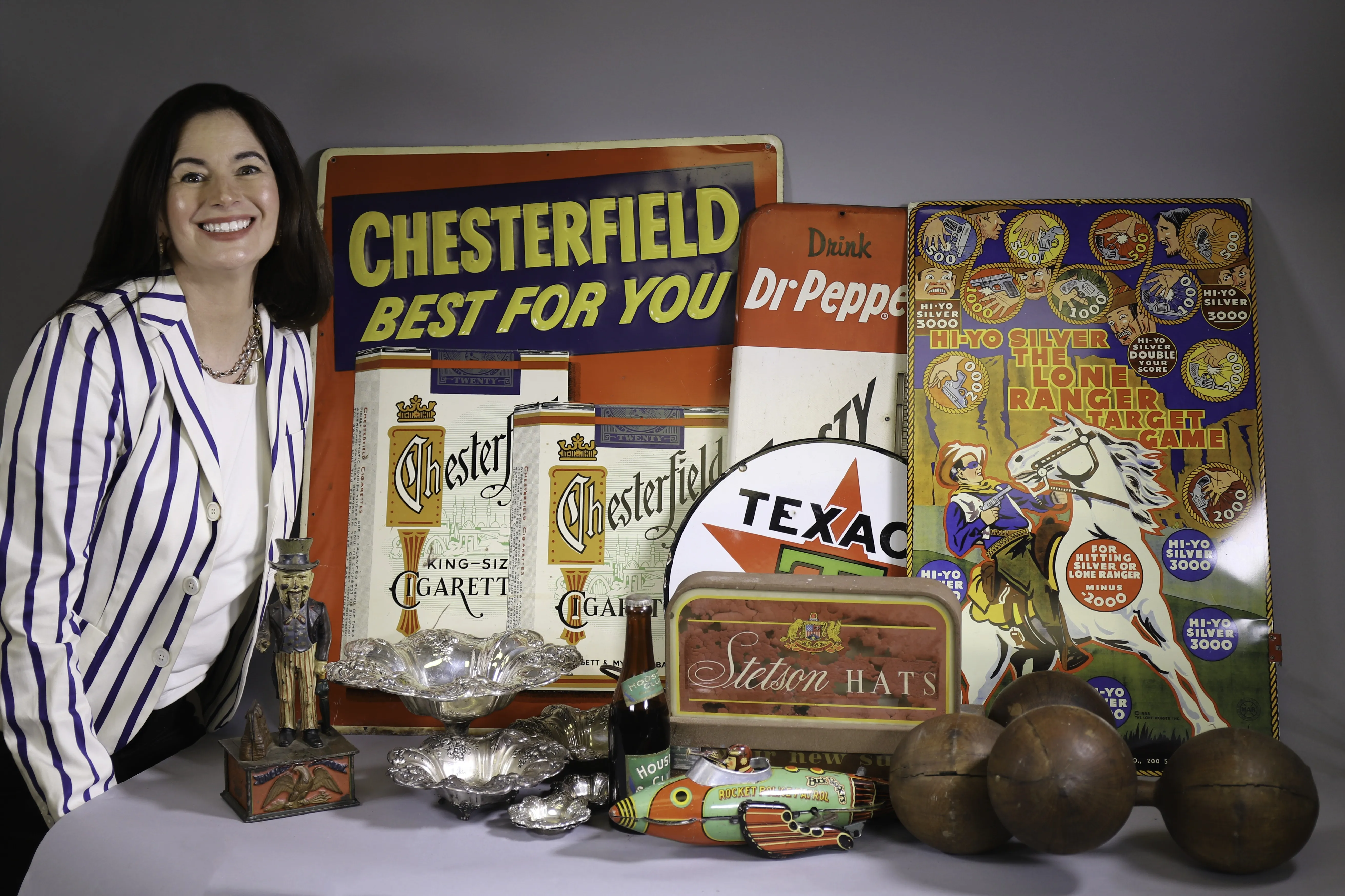 Dominique Kendall seated beside a collection of vintage signs, silver, and estate sale objects.