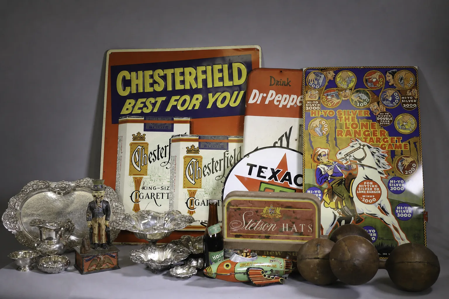Vintage advertising signs and silver serving pieces arranged for an estate sale.