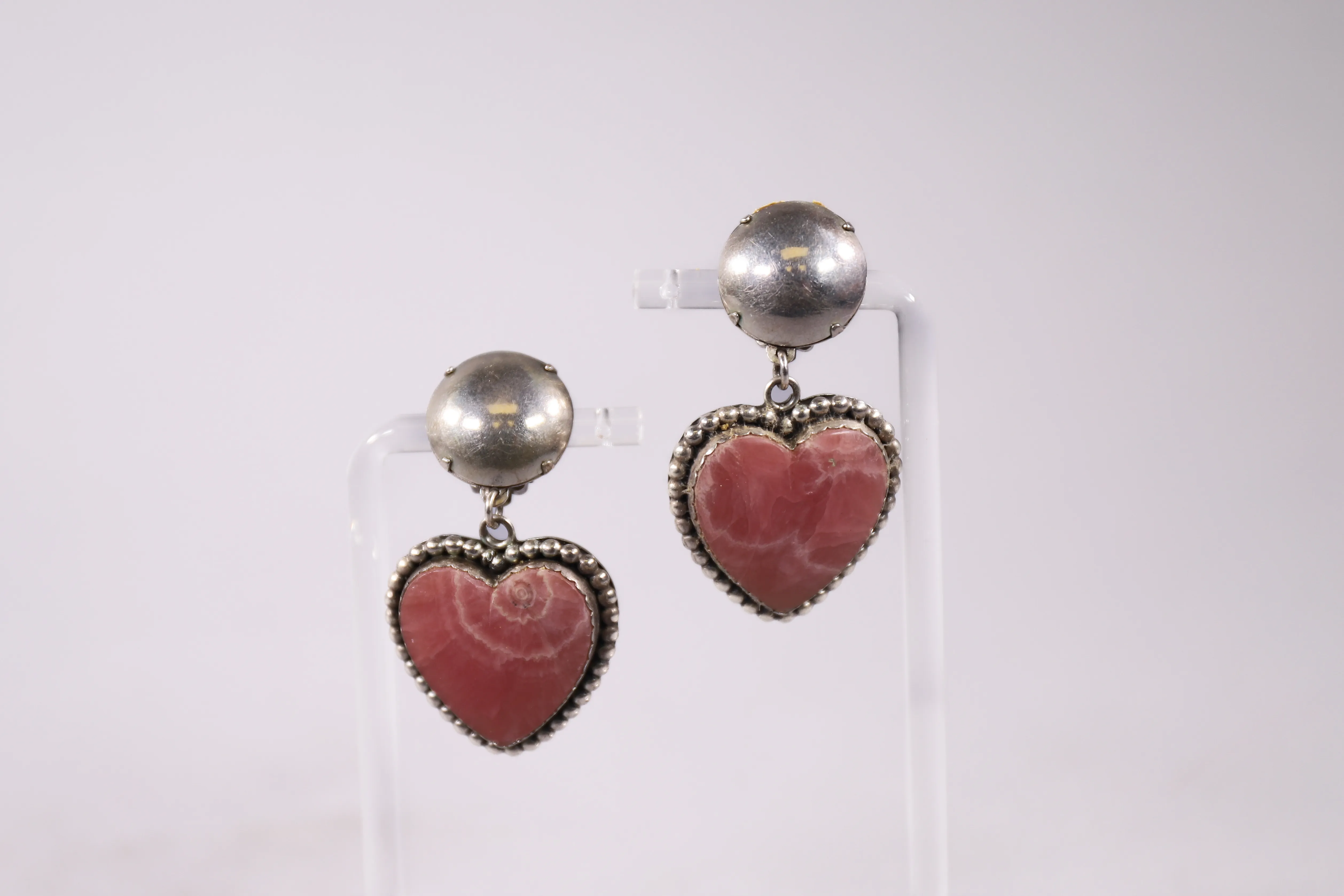 Pink-red heart drop earrings displayed on clear stands.
