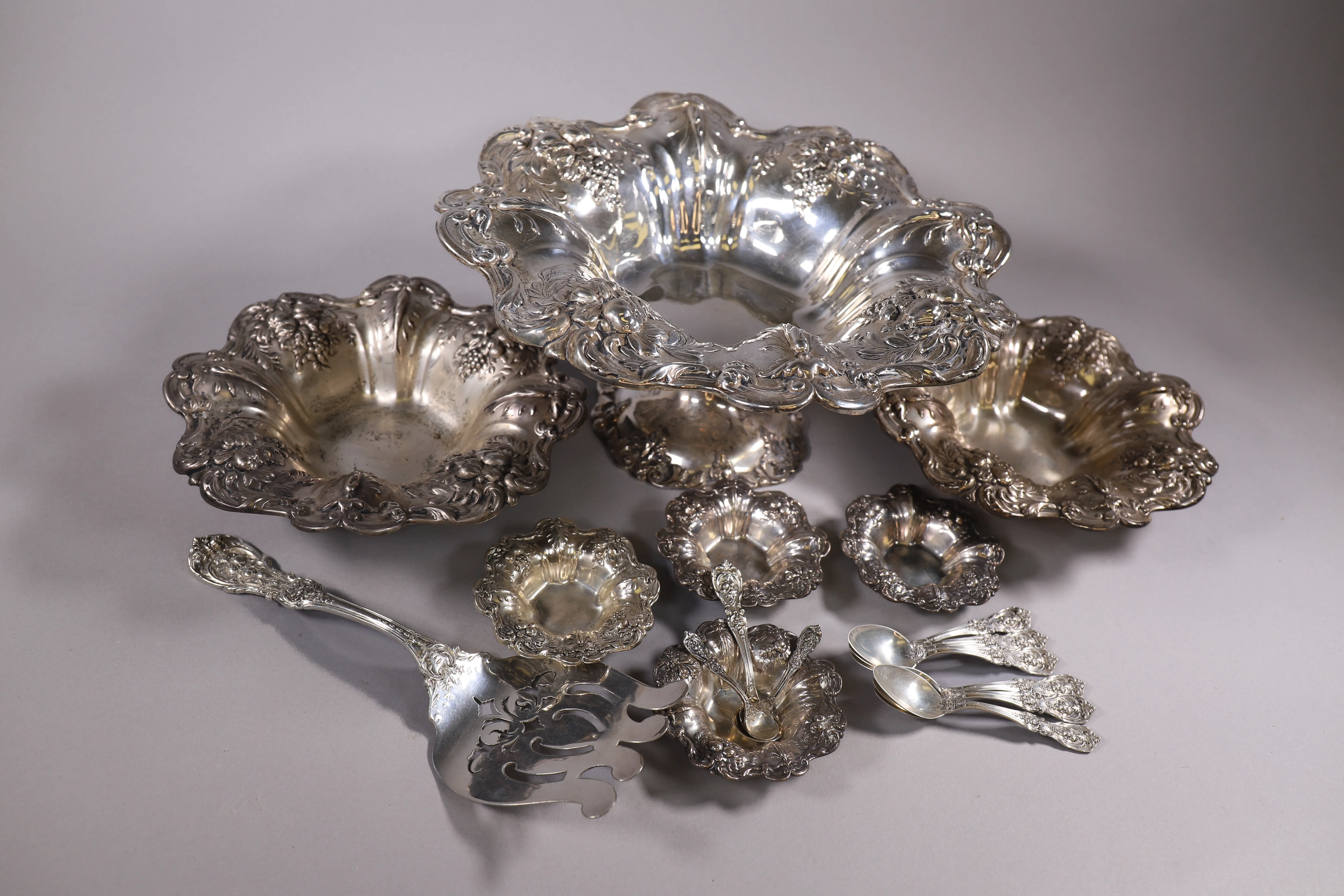 Ornate silver serving pieces and flatware grouped for estate sale staging.